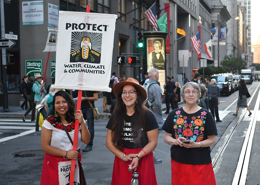 Noemi Tungüi holds up a protest sign and stands beside two other protesters on a street in San Francisco.