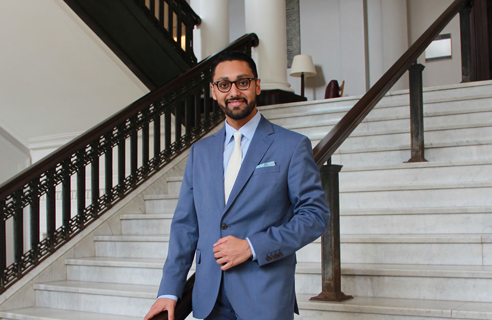 Omar Ullah, CSUN's 2002 Wolfson Scholar, wears a blue suit and tie, and stands on the stairs inside a Harvard Medical School building.