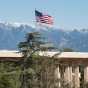 The American flag flies at the top of the flag pole on the roof of the Oviatt Library, with snow-capped mountains in the background.
