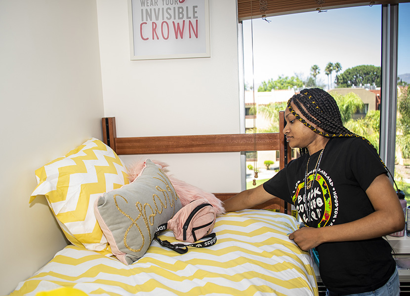 A student leans over her dorm bed to adjust her decorative pillows.