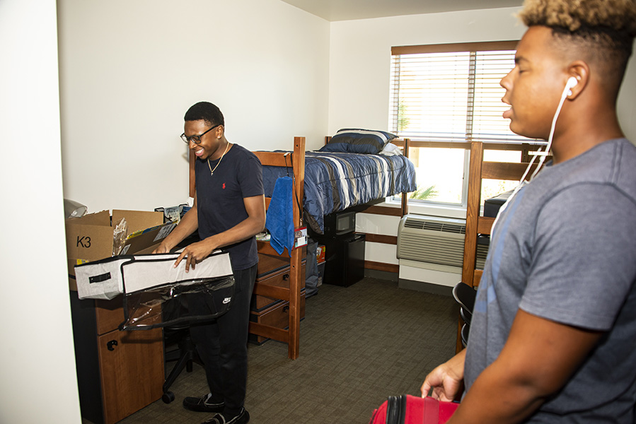 Two roommates enjoy some music as they unpack their belongings in their dorm room.