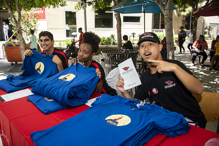 Three staff members sit at a table with a red tablecloth and distribute blue T-shirts to welcome new residents.