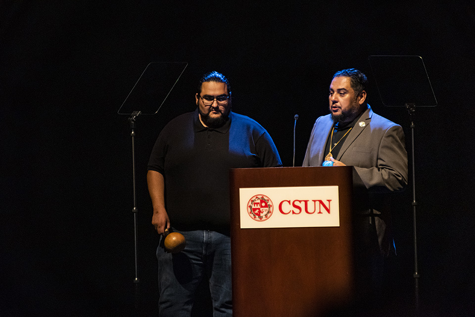 Two men stand at a podium on a dark stage at The Soraya