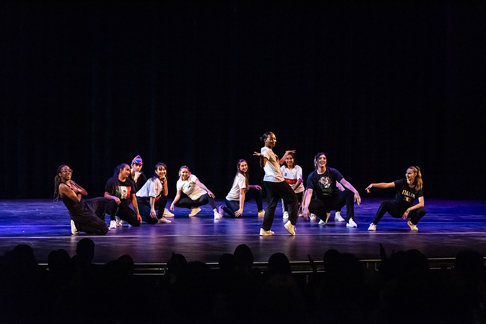 Dance students strike a pose against a dark backdrop on stage.