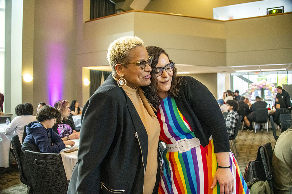 Debra Hammond, USU executive director, hugs an alumna in a rainbow-striped dress.