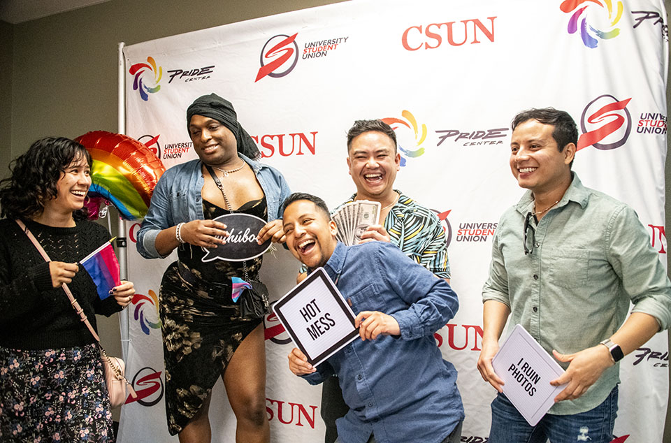 Alumni and students laugh and hold up signs at the CSUN Pride Center gala photo booth.