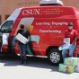 Three CSUN faculty and staff members stand in front of the red-and-white van for CSUN's Family Focus Resource Center, next to a pile of diaper boxes.