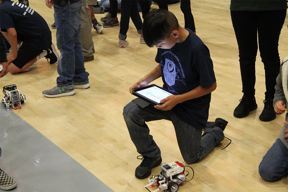 A student on one knee uses a tablet to control his robot.