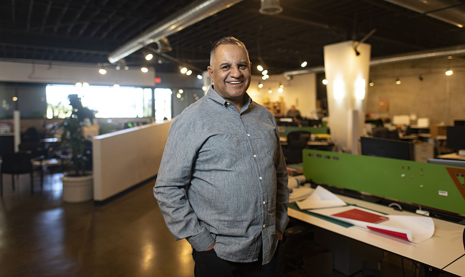 Alumnus Ravi Sawhney stands in the open design studio of his company headquarters, RKS, in Thousand Oaks. Behind him are drafting tables and large computer monitors.