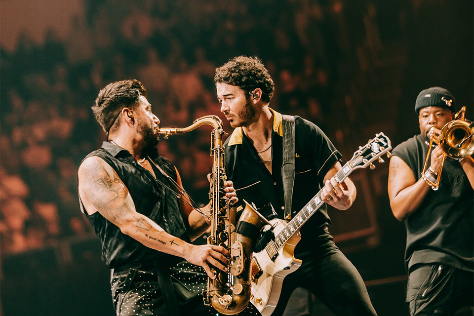 Fabian Chavez plays the tenor saxophone while singer Kevin Jonas plays the guitar interacts.