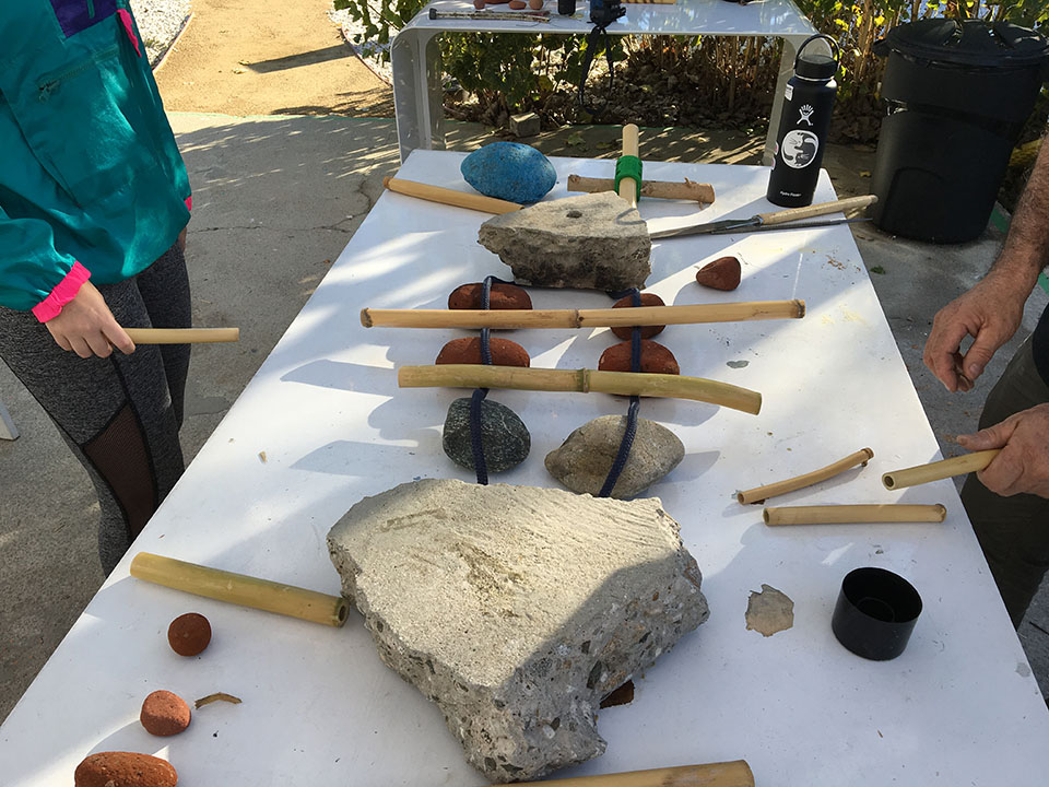 A table displaying percussion instruments made from cane plant reeds and rocks, from the LA River.