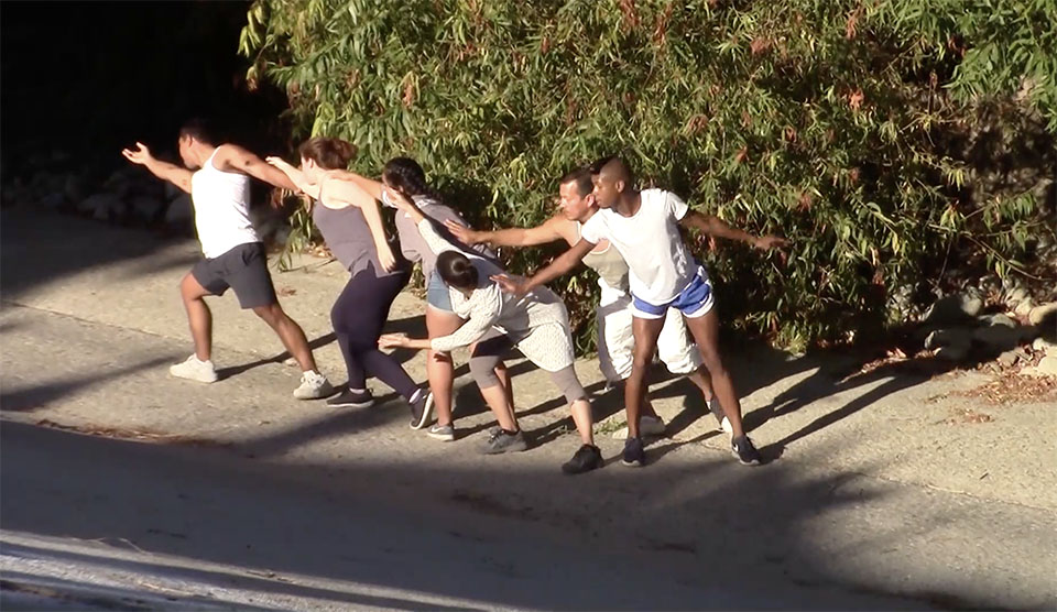Six student dancers - both young men and women - performing a group dance, while standing on a bank of the LA River.