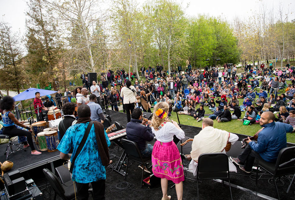 Musicians play on a stage in front of an audience that is seated on grass.