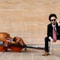 Musician Rodrigo Moreno sits in a chair, wearing sunglasses, next to his string bass.