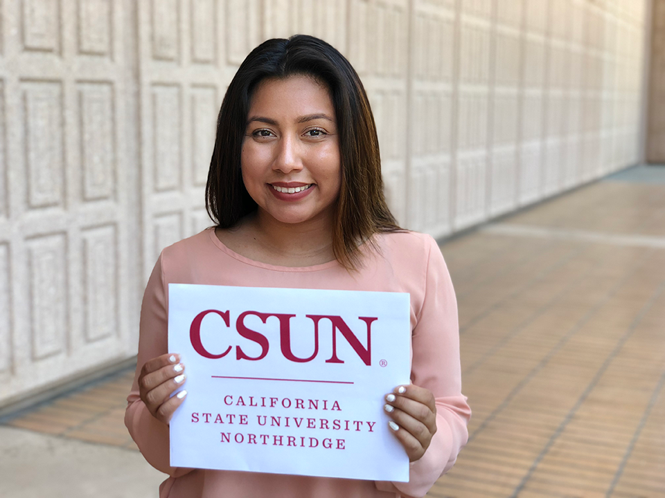 CSUN student, Roxana Lesso standing with a CSUN sign in front of the Oviatt Library.