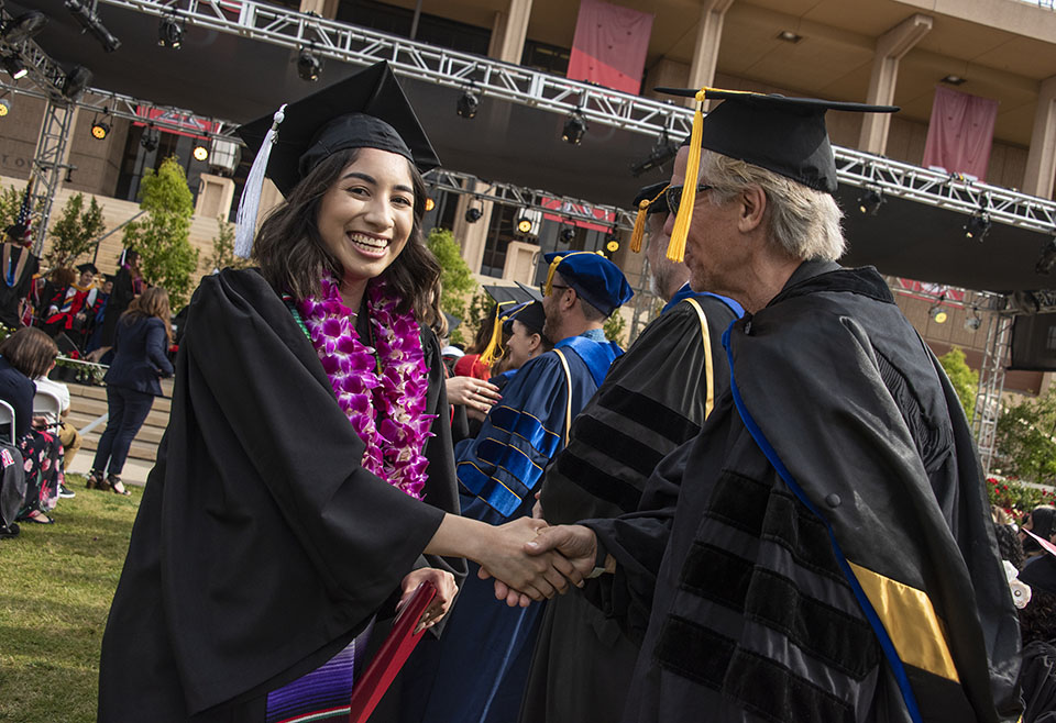 Smiling college graduate shakes a faculty member's hand during a graduation ceremony.