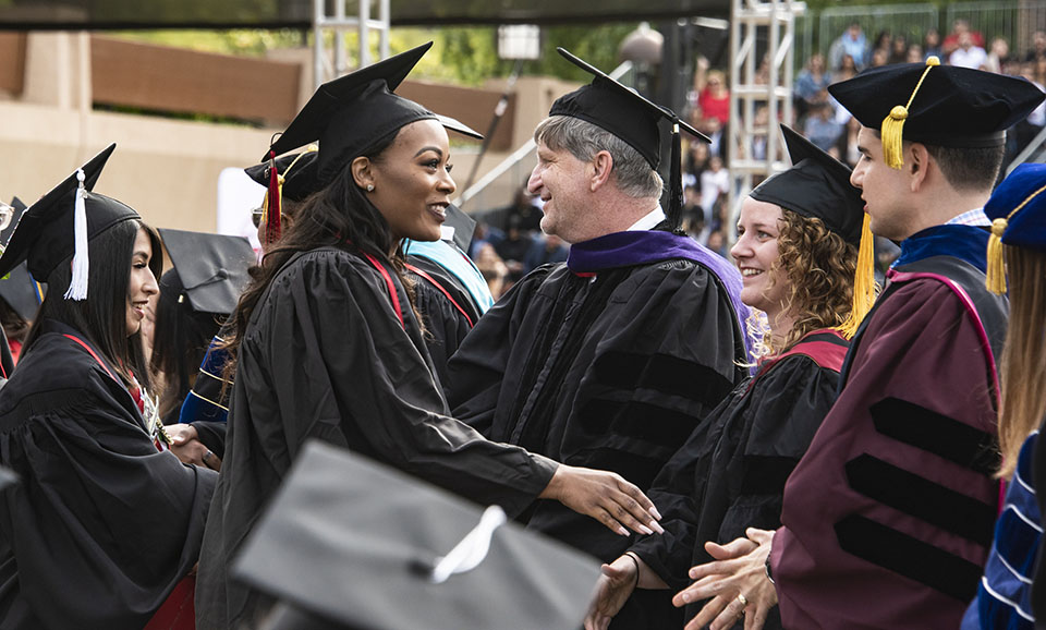 Smiling college graduate shakes a faculty member's hand during 2019 CSUN commencement ceremony.