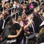 A crowd of college graduates smile and cheer during a graduation ceremony.