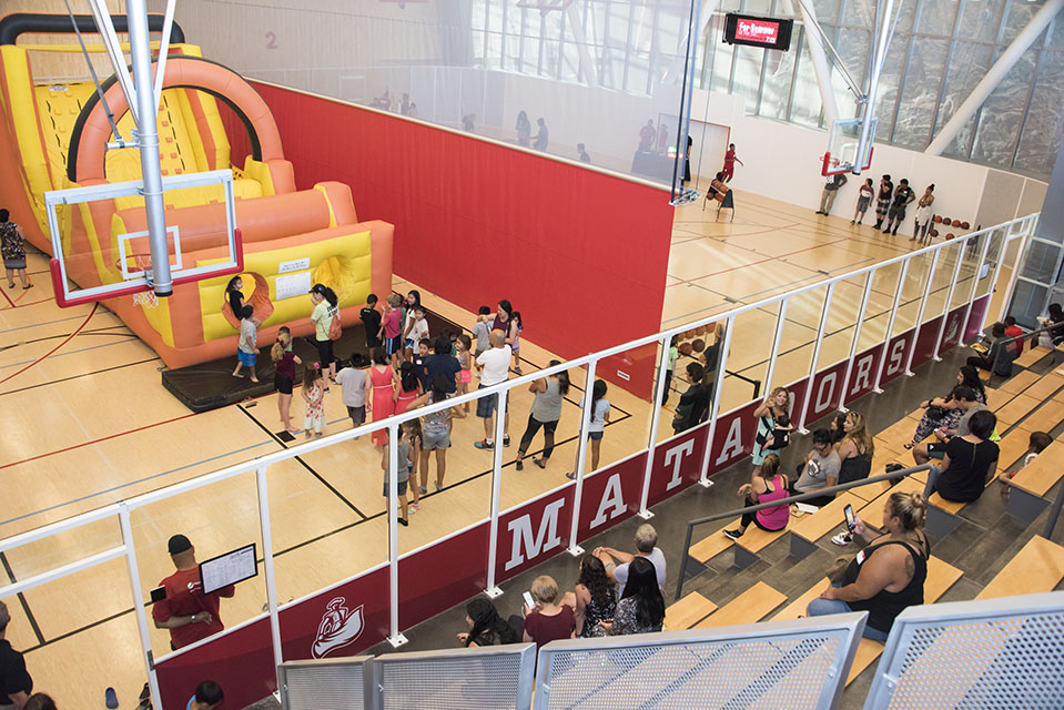 Children line up to run in the inflatable obstacle course as parents watch. Across the court, attendees participate in the 3-point contest.