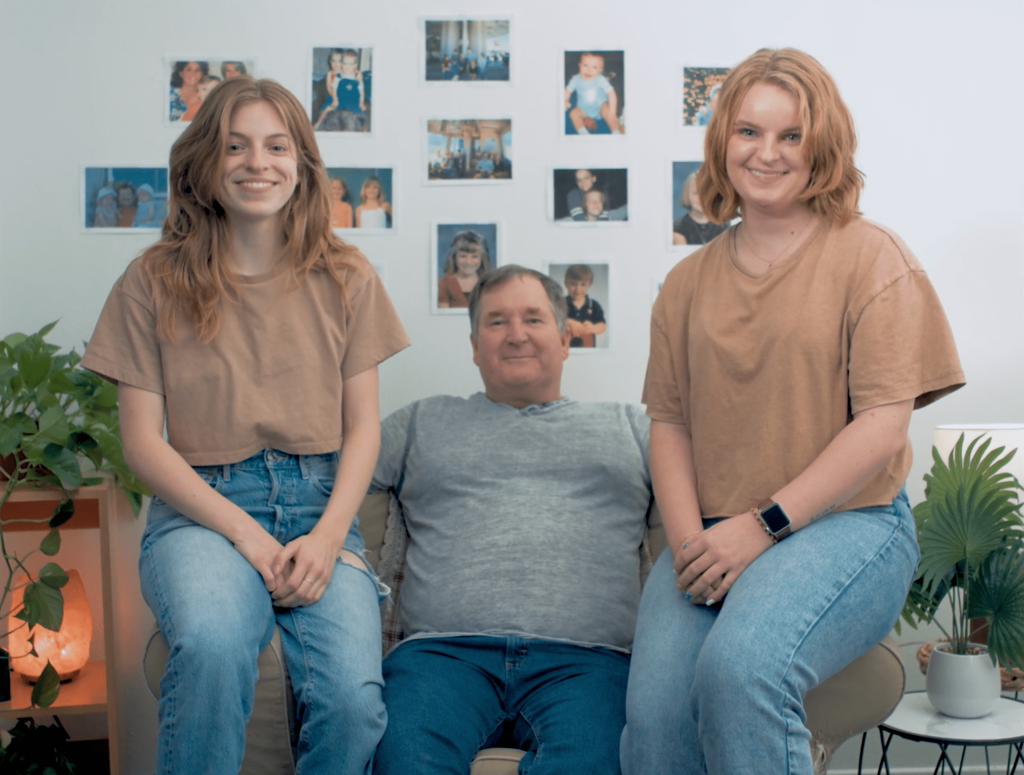 Hailey, Steve and Sara Sims are all seated on a bench smiling at the Camera. The image is a still taken from the short film '#2276.'