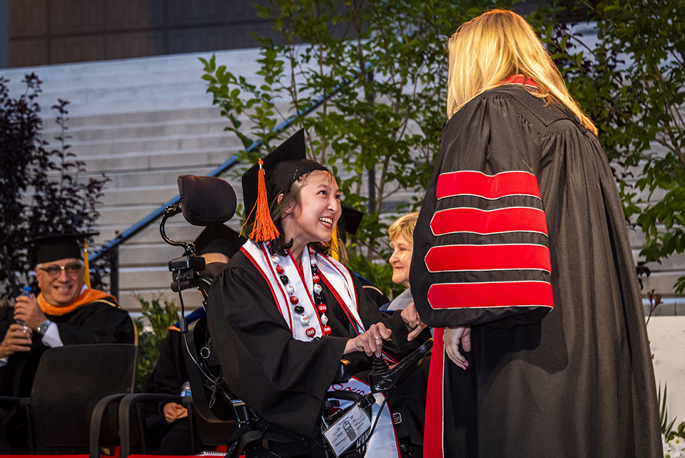 President Erika D. Beck gives a fist bump and greets 2022 Wolfson Scholar Megan Ngo, as she crosses the stage in her motorized wheelchair, at Commencement 2022.