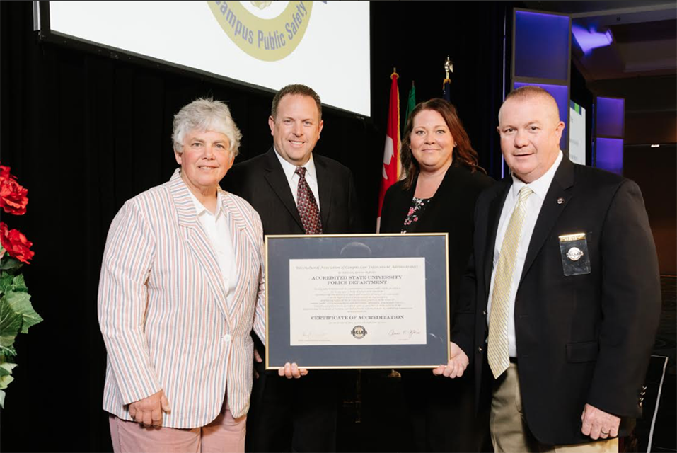 Standing From left to right Chief Anne P. Glavin, Captain Scott VanScoy, Jessica Luedtke (Accreditation Commission Chair, IACLEA), Chief David Bousquet (Immediate Past-President of IACLEA) holding the accreditation award.