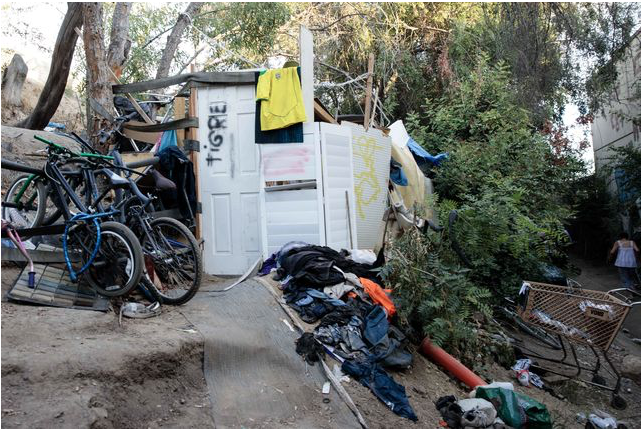 A homeless encampment behind the 405 freeway with bikes and shopping carts and a door.