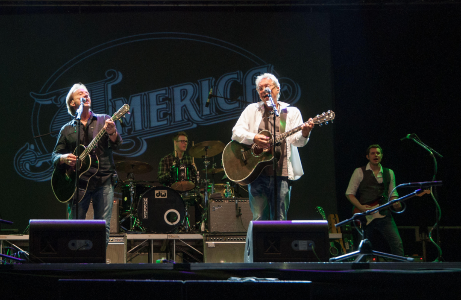 America band members Bill Worrell (far right), Gerry Beckley (center guitar) and Dewey Bunnell (far left) playing on stage together.