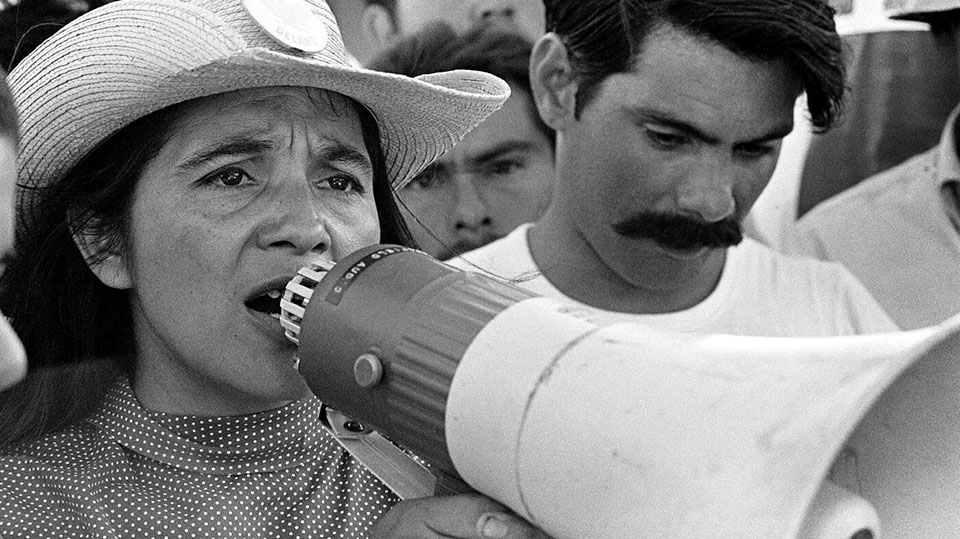 Vintage black-and-white photo of Dolores Huerta directing United Farm Workers marchers in 1969.