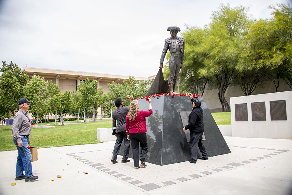 Three staff members place roses on the matador statue.