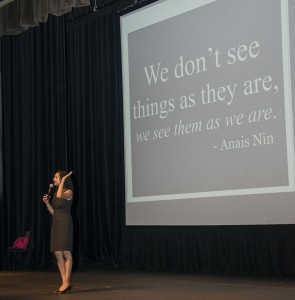 Sumun Pendakur of USC stands in front of a large screen that displays a quote by Anais Nin: "We don't see things at they are, we see things as we are." Pendakur is holding a microphone.