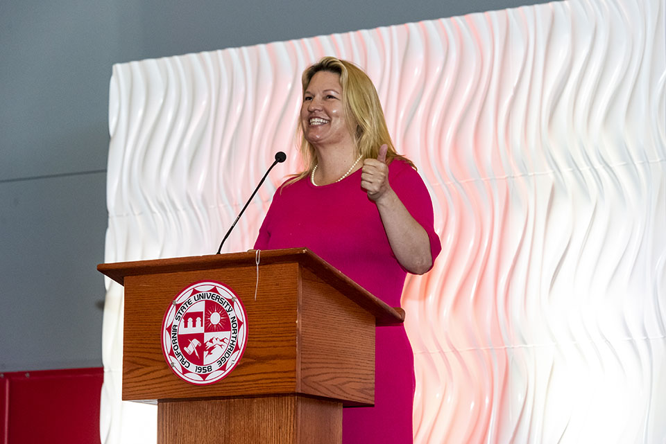 President Erika D. Beck stands at the podium and gives a thumbs up while she thanks the staff and faculty.