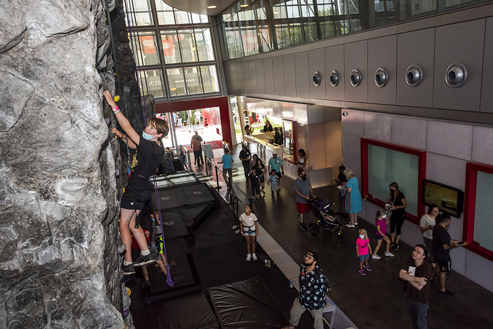 A young climber takes on the SRC Rock Wall as others watch below.