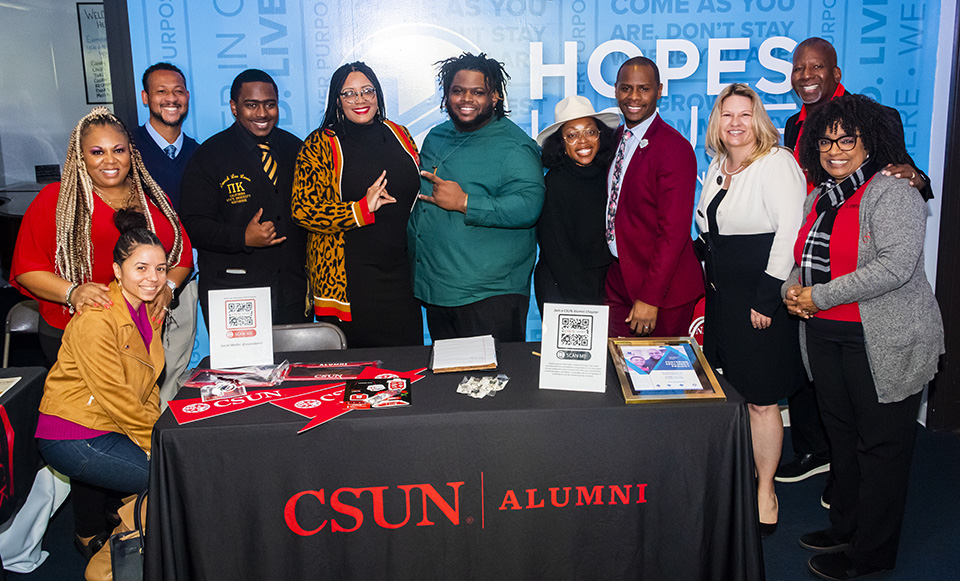 CSUN President Erika D. Beck stands with a group of CSUN leaders, alumni and students at a table decorated with a "CSUN Alumni" banner and Black Alumni Association materials.