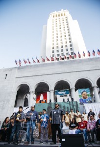 Tataviam tribal leaders and children stand on a stage in front of Los Angeles City Hall, giving a blessing for Indigenous Peoples Day.