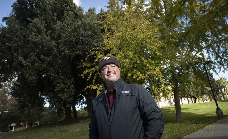 Tom Case stands smiling before trees and grass
