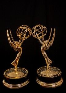 Two Emmy statues facing each other against a black background. 
