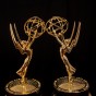 Two Emmy statues facing each other against a black background.