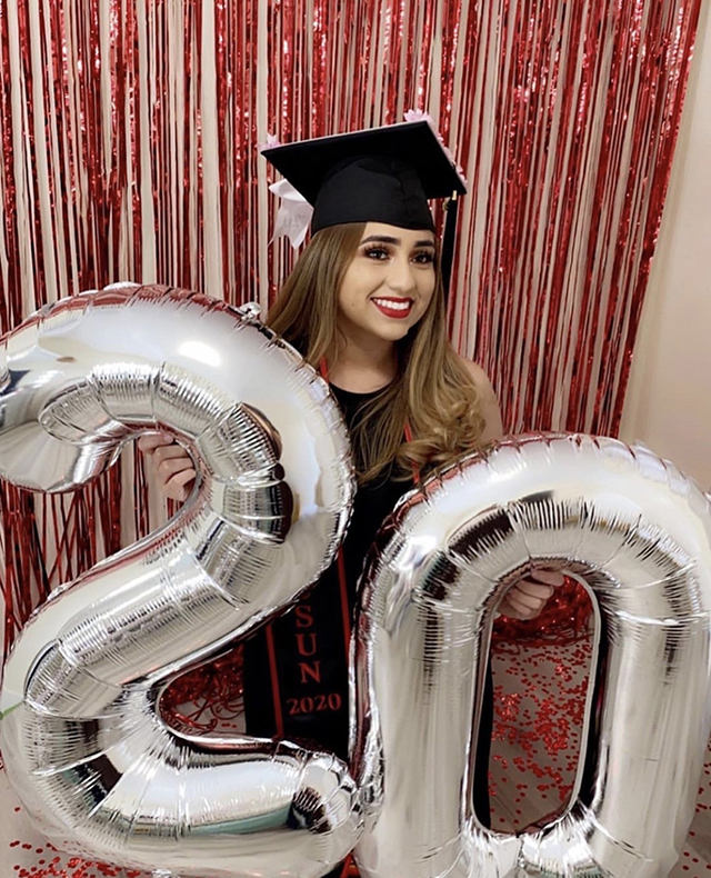 A CSUN student in graduation cap and gown poses with 2020 balloons.