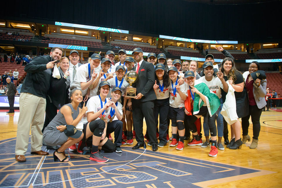 Players and coaches at midcourt with the trophy.