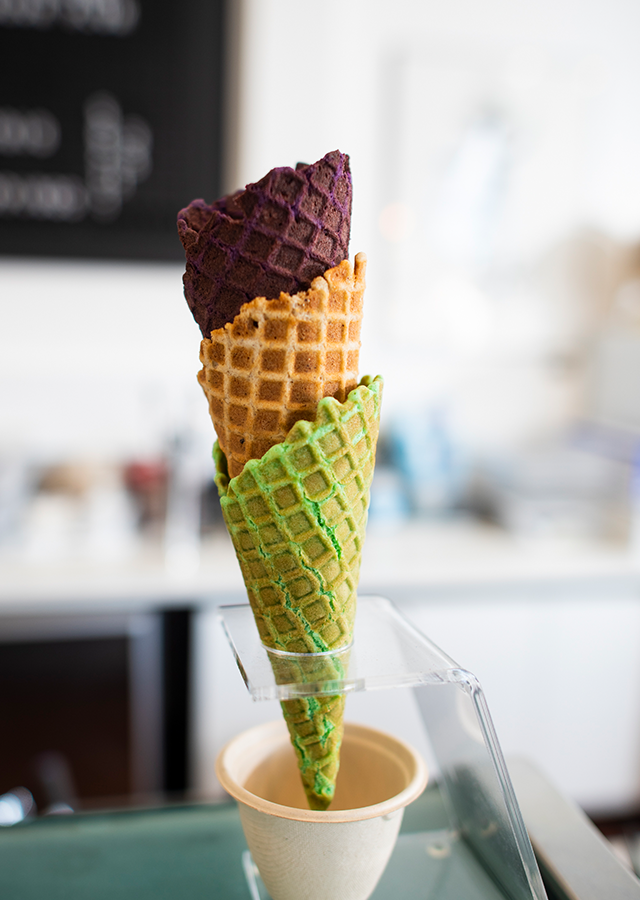 Three handmade waffle cones are stacked on a stand on the store counter.