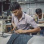 Two men sit at sewing machines, working on bluejeans in a clothing factory in Mumbai, India.