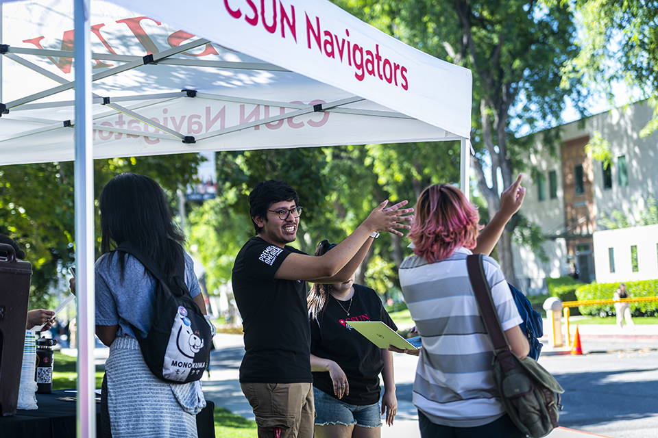 A staff member points out the direction to a student under a CSUN Navigator pop up tent.