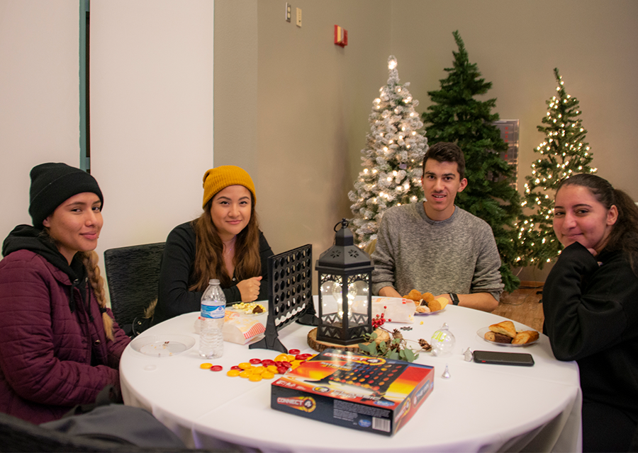 Four students with their dessert plates sit around a table to play a board game.