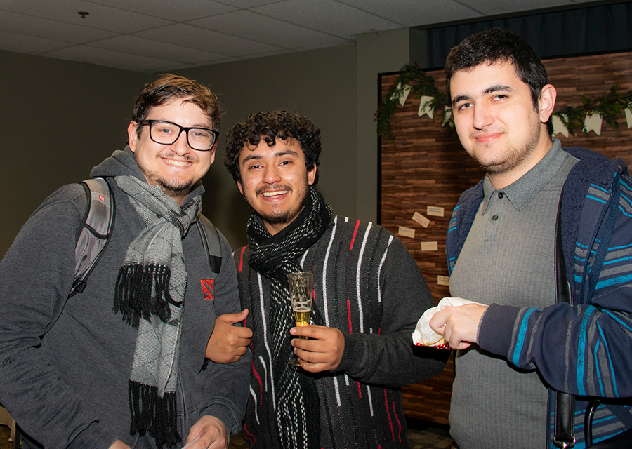 Three CSUN students in sweaters and scarves, with one holding a pack of popcorn and another holding a glass of apple cider.