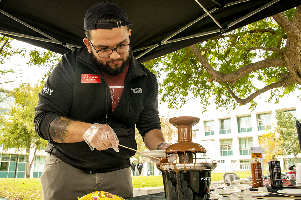 Students Outdoor Adventures Coordinator Joey Cortez dips a treat on a stick into the chocolate fondue fountain.