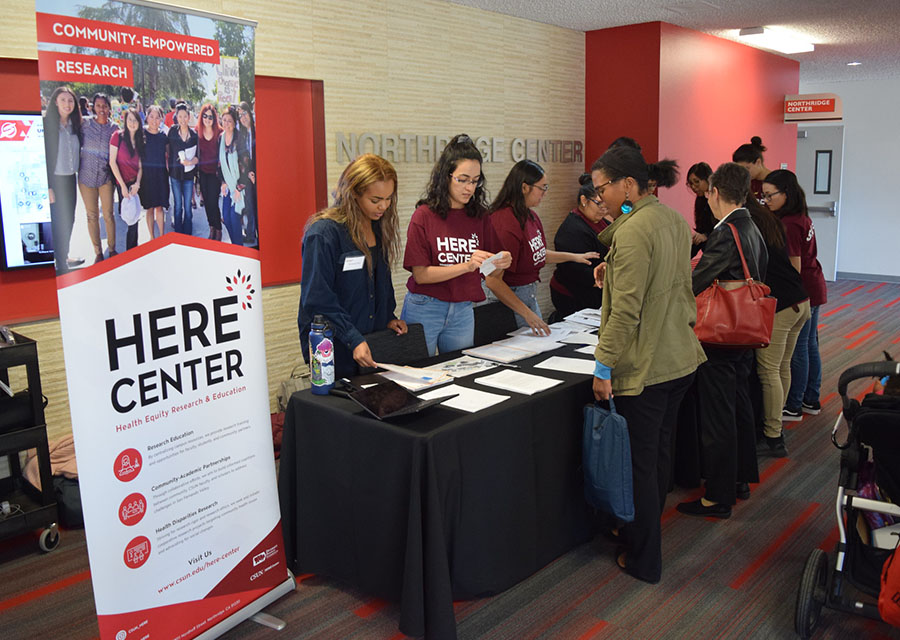 Attendees standing at a table by a HERE Center poster