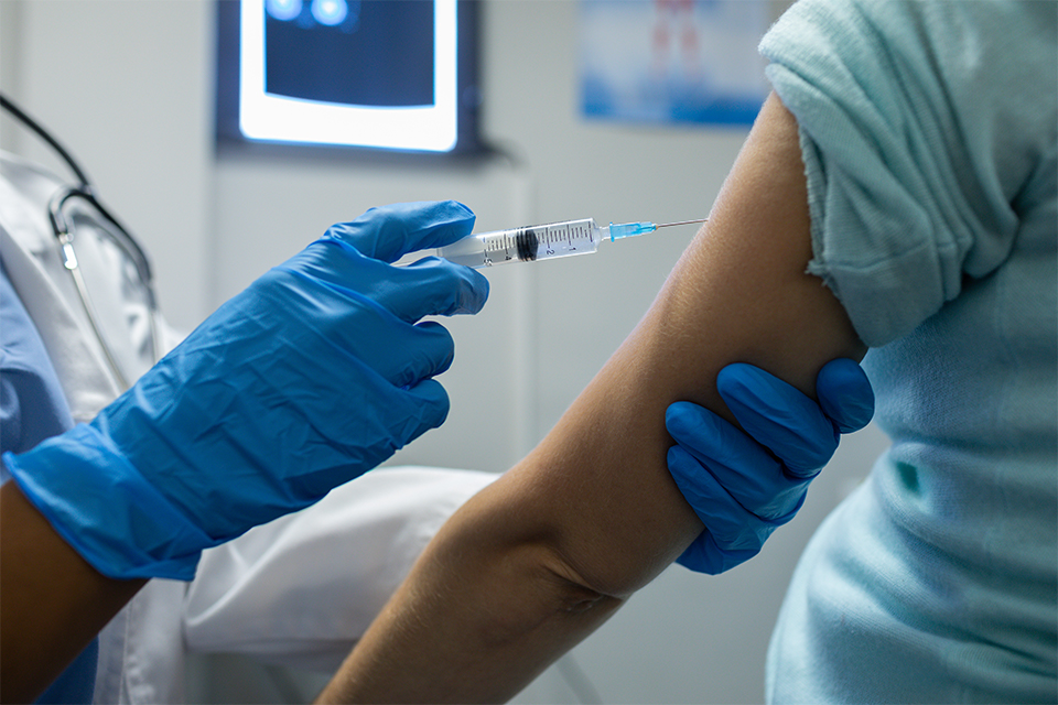 A health care provider in gloves injects a vaccine into a patient's arm.