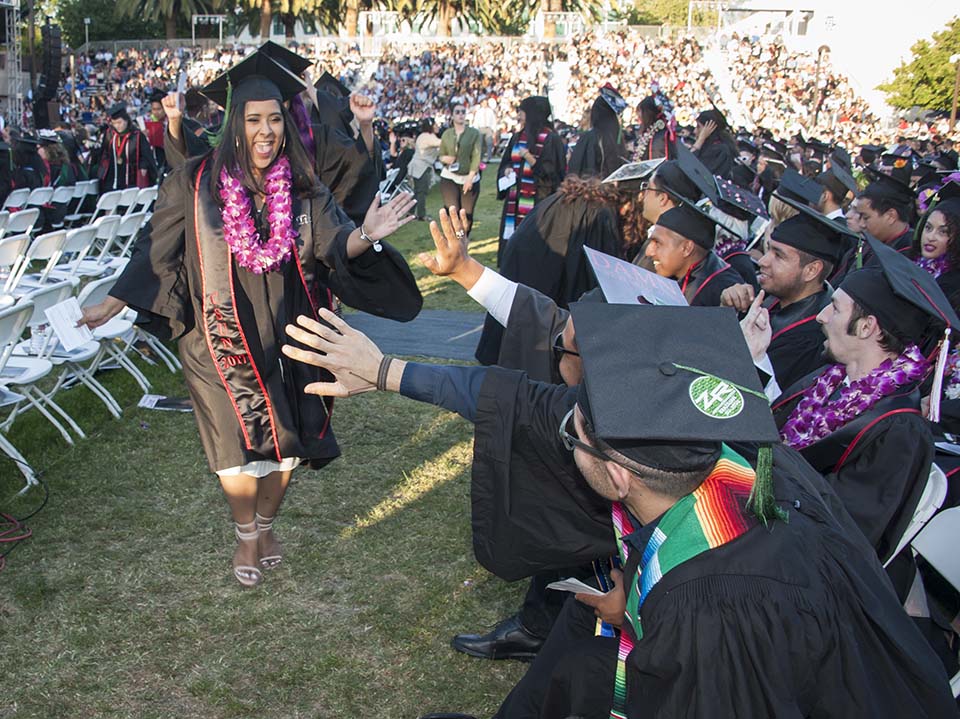 A CSUN graduate runs to high-five a row of classmates.