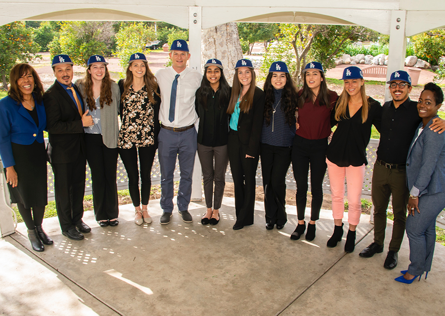 The ten Campanella/Dodgers Scholarship recipients, all wearing their Dodgers hats, pose for a photo with Joni Campanella-Roan, daughter of Roy and Roxie Campanella, and LA Dodgers Foundation executive director Nichol Whiteman outside the Orange Grove Bistro in February 2019.
